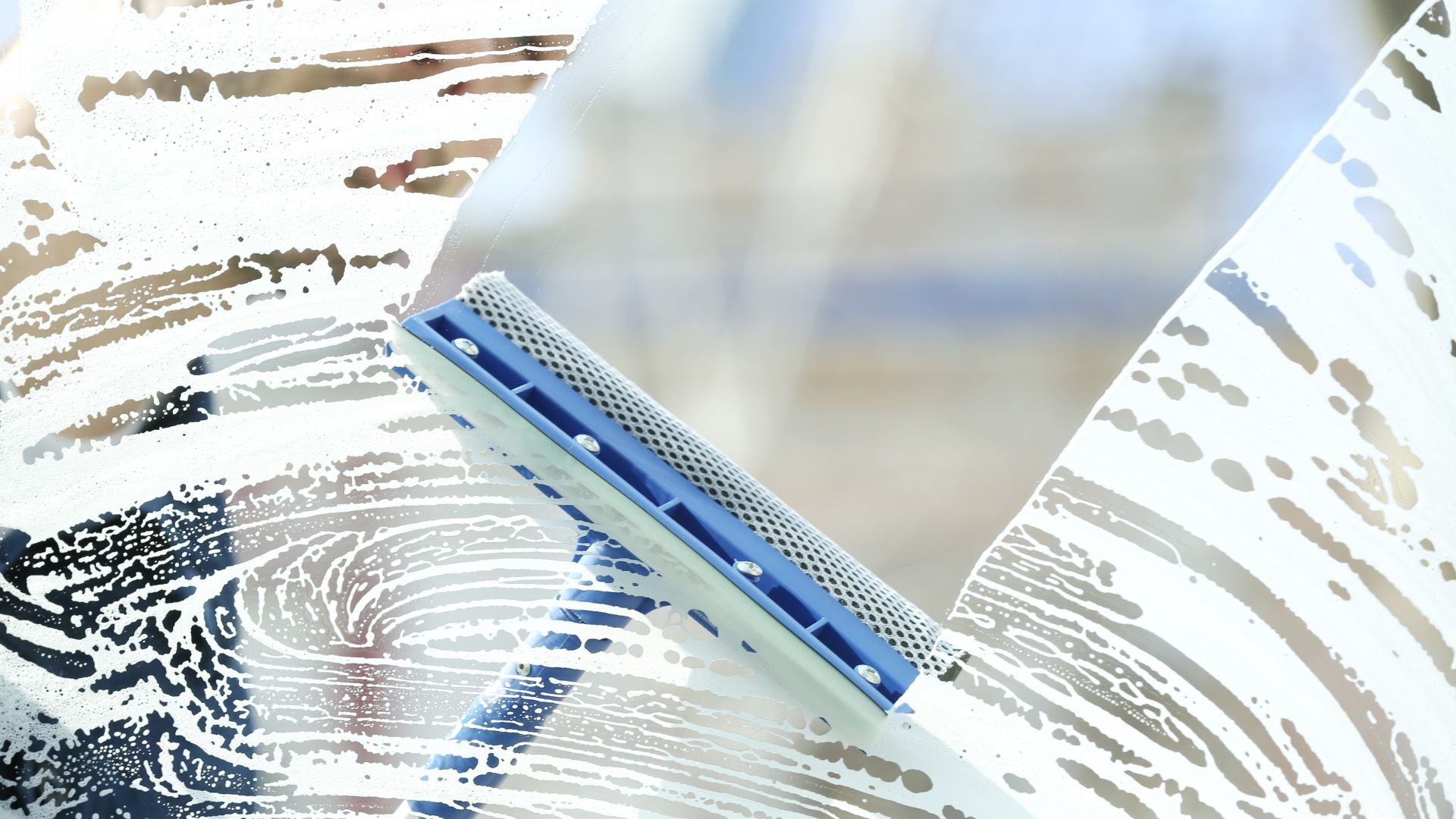 Blue squeegee cleaning soapy window with blurred background