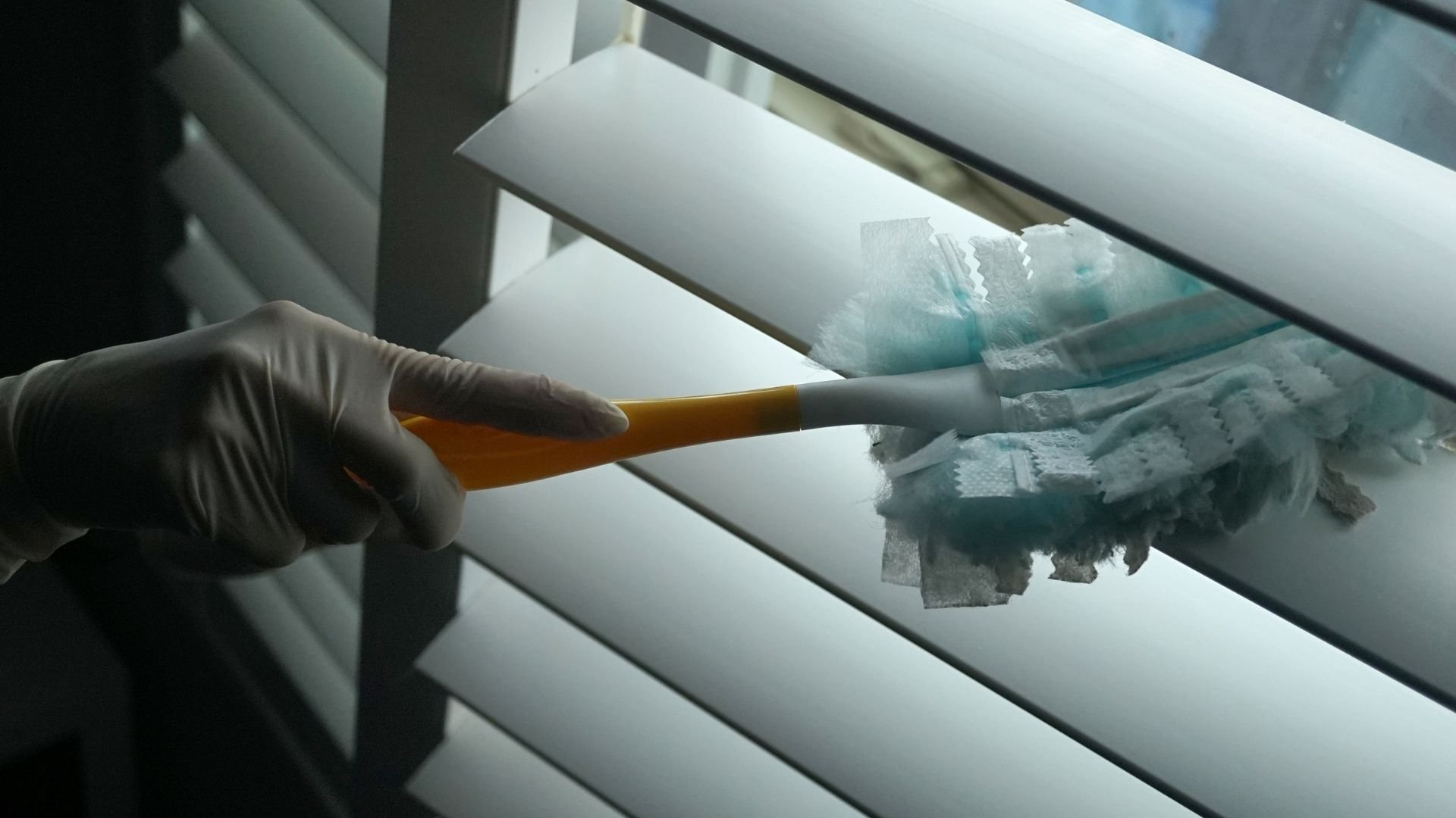 Gloved hand holding cleaning brush near window blinds