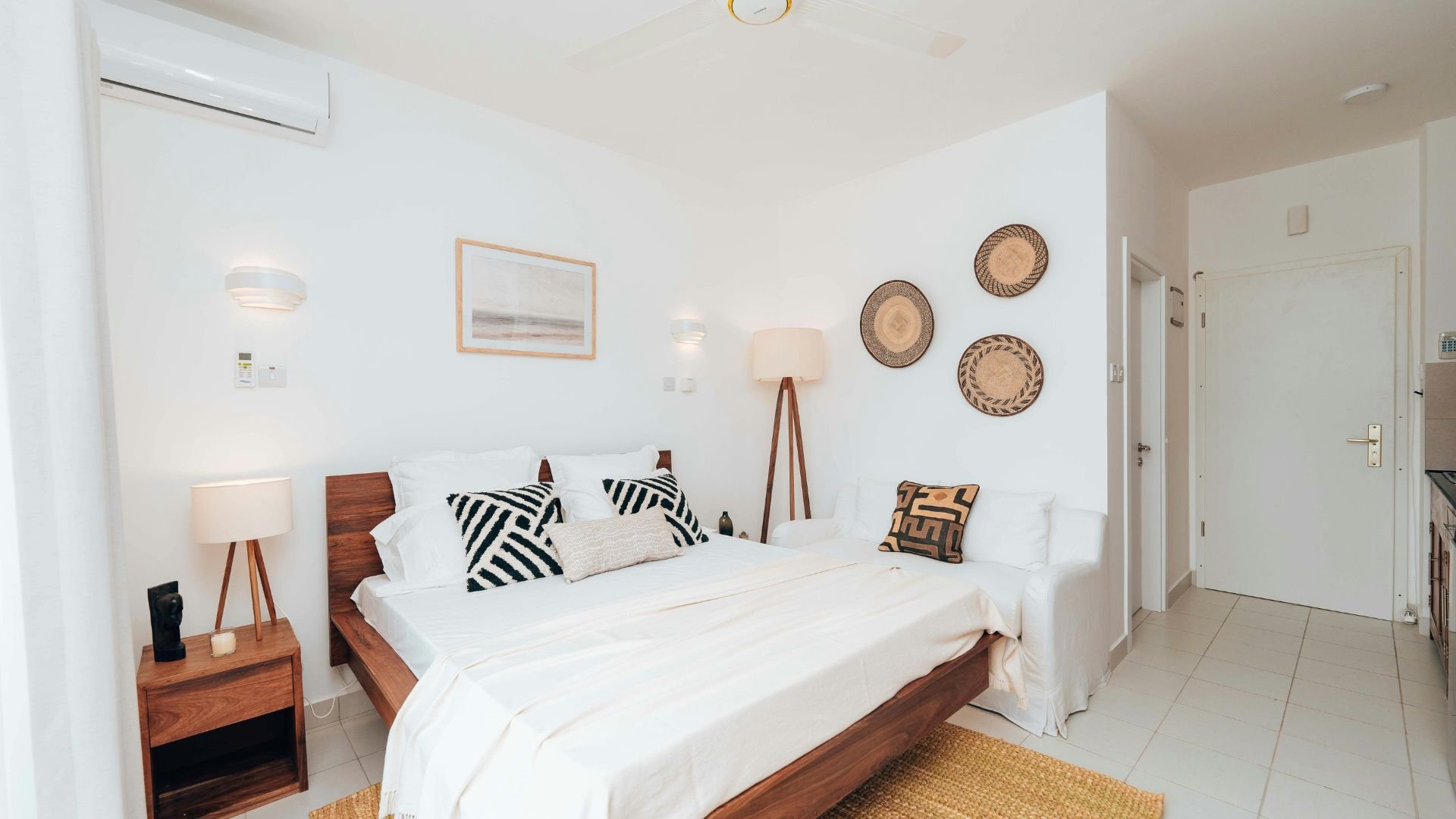 Minimalist bedroom with wooden bed, white linens, and decorative woven wall baskets