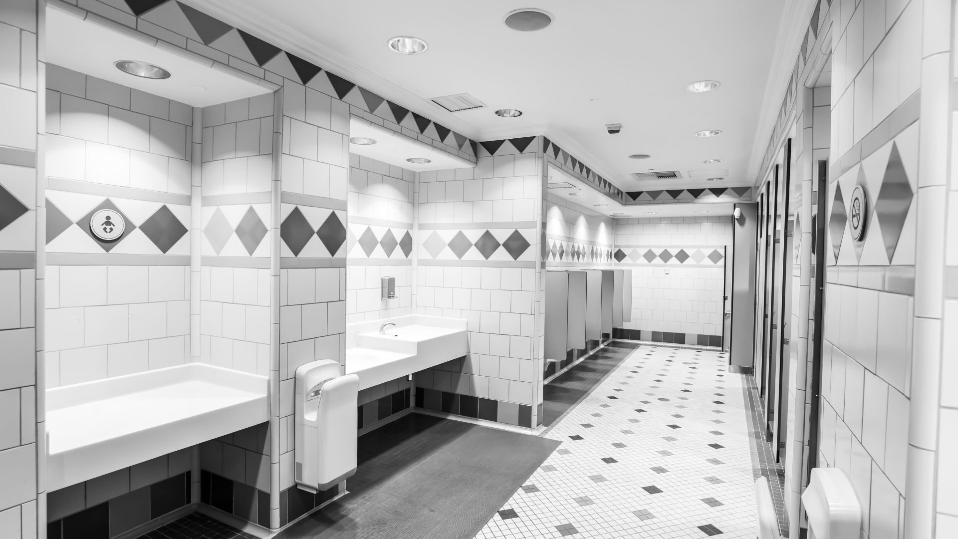 Clean public restroom with white tiles, sinks, and geometric black and white design